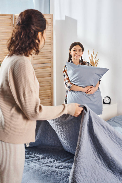 Una niña sostiene una almohada, mostrando un momento tierno entre una madre y su hija en casa. - Foto, Imagen