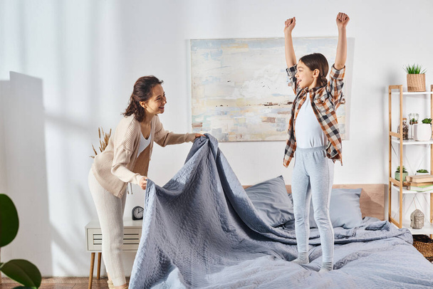 moeder en dochter, staand op een bed met een blauwe deken, samen tijd doorbrengen. - Foto, afbeelding