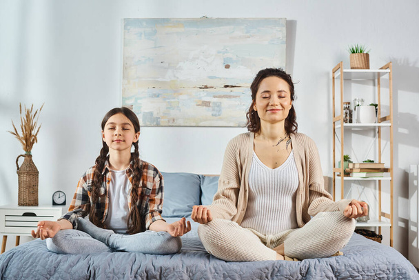 Eine Mutter und eine Tochter verbinden sich, wenn sie gemeinsam Yoga auf einem gemütlichen Bett zu Hause praktizieren, was Verbindung und Wohlbefinden fördert. - Foto, Bild