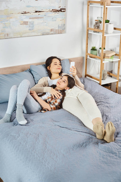une mère et sa fille, se blottissant et se relaxant sur un lit confortable dans une étreinte chaleureuse et aimante. - Photo, image