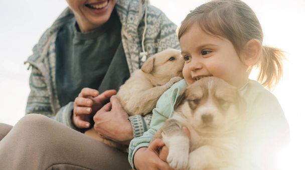 Yeni yavru köpeklerini kucağında tutan ve okşayan genç bir kadın ve kızının güzel portresi. Arkadaşlık ve bakım kavramı - Fotoğraf, Görsel