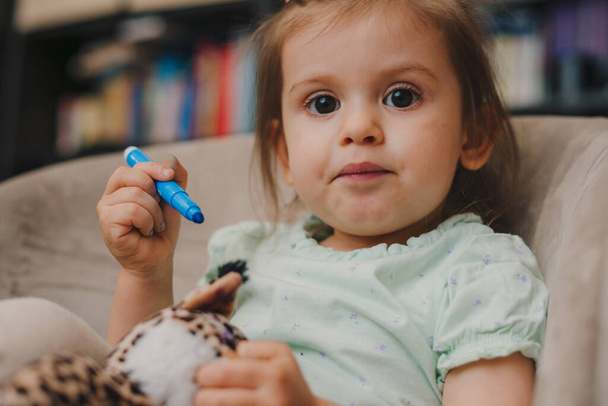 Expressions sur le visage d'une fille douce tout en jouant à la maison avec marqueur bleu. - Photo, image