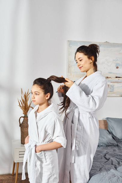 A brunette mother and her little daughter, both in white bath robes, standing together in a heartwarming moment. - Foto, Imagem