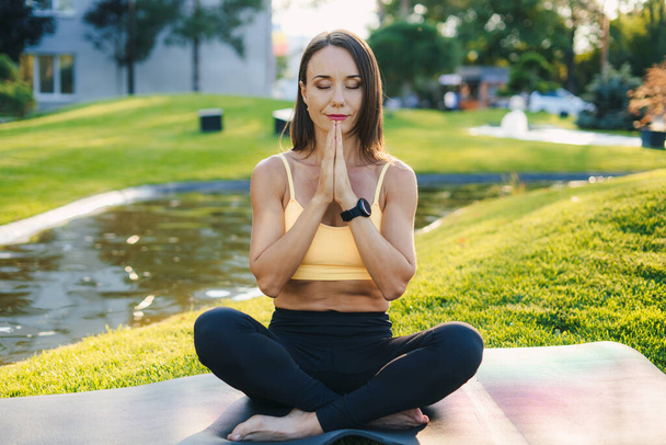 Beautiful adult woman doing breathing yoga exercise in the summer park. Caucasian female meditation pose, healthcare. - Photo, Image