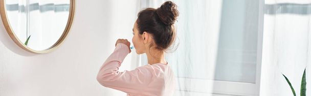 Une préadolescente brune se tient dans une salle de bain moderne, brossant des dents devant un miroir. - Photo, image
