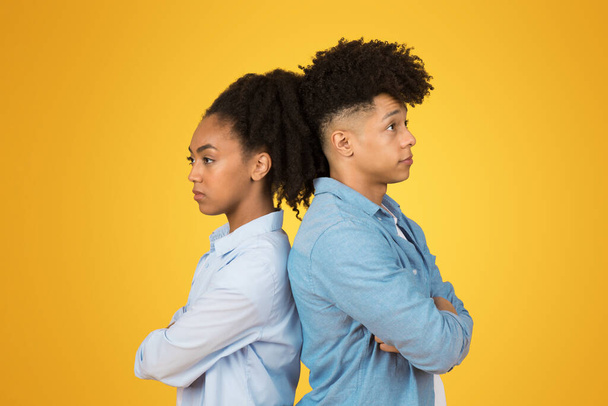 悲しい怒りのミレニアル世代のアフリカ系アメリカ人男性と女性は,活気に満ちた黄色の背景に対して,腕を交差させ不快な表情で後ろに立ちます. 愛,関係の問題 - 写真・画像