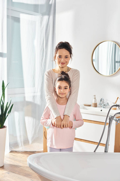 A brunette woman and her preteen daughter stand in front of a bathtub, engaging in their beauty and hygiene routine. - Photo, Image