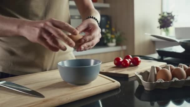 Lähikuva laukaus tunnistamaton mies halkeilua kaksi munaa kulhoon keittiön pöydälle, kun ruoanlaitto aamiainen kotona - Materiaali, video
