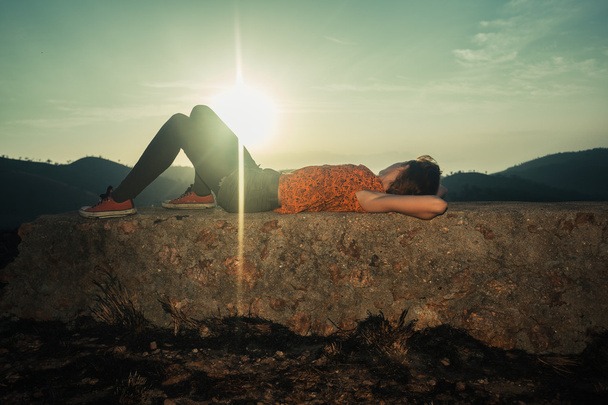 Femme couchée sur un rocher insolite au lever du soleil
 - Photo, image