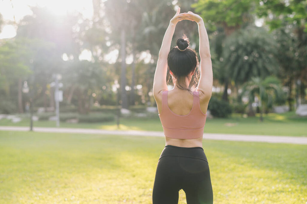 wellness i zdrowy styl życia portret Azjatki 30s w różowej odzieży sportowej. przygotowanie i rozciągnięcie mięśni ramion przed zachodem słońca w parku. sprawność zewnętrzna i zrównoważona koncepcja życia. - Zdjęcie, obraz
