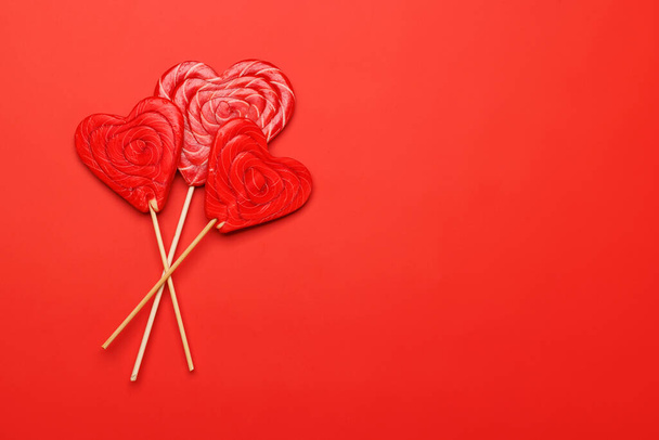 Lecca lecca-lecca cuore: Dolci prelibatezze su sfondo rosso con spazio di testo. Flat lay biglietto di San Valentino - Foto, immagini