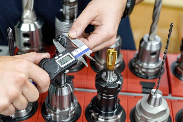CNC-työstökoneen työntekijä mittaa leikkuutyökalun kaliiperilla jyrsin- ja sorvauskoneiden jatkokäsittelyä varten. - Valokuva, kuva
