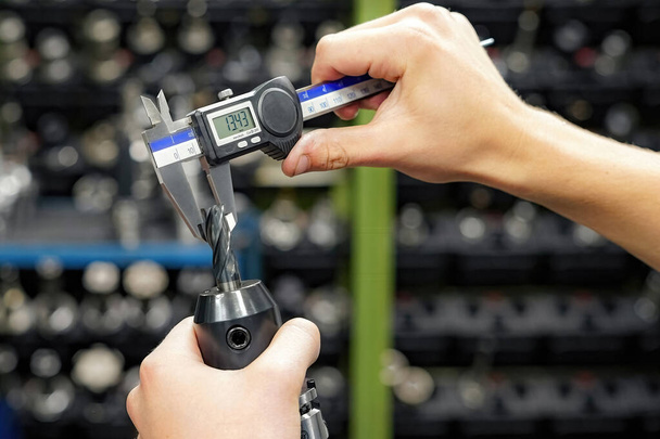 CNC-työstökoneen työntekijä mittaa leikkuutyökalun kaliiperilla jyrsin- ja sorvauskoneiden jatkokäsittelyä varten. - Valokuva, kuva