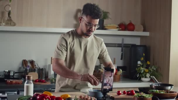 Voedsel blogger kraken ei en het toevoegen van melk om te bowlen tijdens het filmen video recept van ontbijt met mobiele telefoon op statief in de keuken - Video
