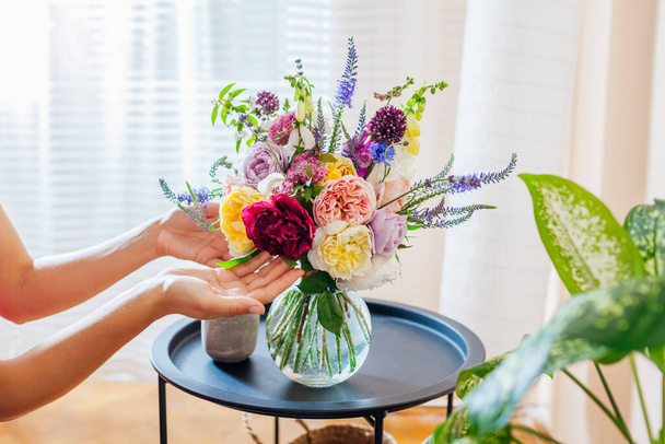 Mujer organiza ramo de rosas flores en jarrón transparente en la mesa. El cuidado de la decoración interior y de verano en el hogar. De cerca. - Foto, imagen