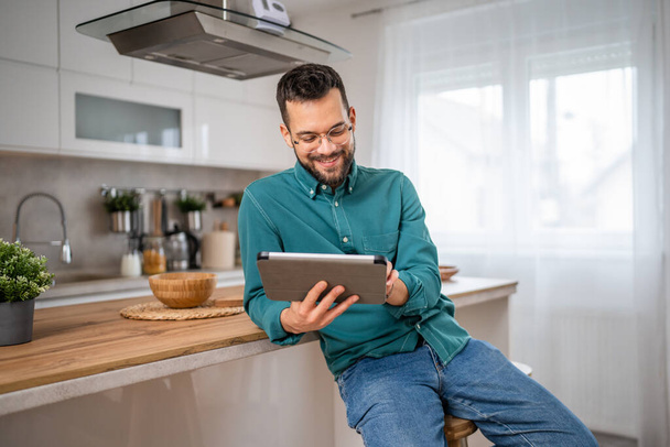 Een man volwassen blanke man houden een digitale tablet werk of surfen op internet vrolijke glimlach thuis zitten vertrouwen dagelijks ochtend routine kopiëren ruimte echte persoon - Foto, afbeelding
