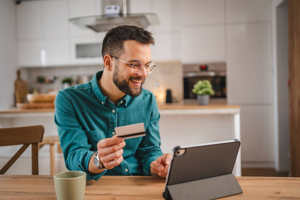 dorosły mężczyzna w domu zakupy online wykorzystanie internetu hold credit card e-banking sklep internetowy e-commerce - Zdjęcie, obraz