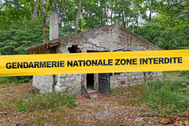 Abandonada casa de pedra na floresta com uma fita policial com escrito em francês "Gendarmerie Nationale zona interdite". - Foto, Imagem