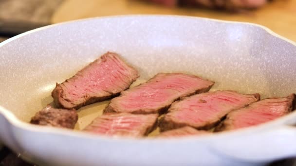 Tongen draaien sappige medium-rare steak strips in een gespikkelde keramische koekenpan. - Video