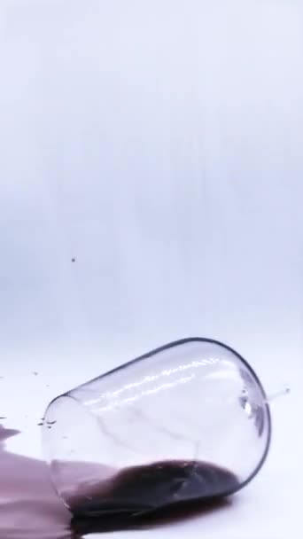 Gota accidental de vidrio con vino tinto se rompe en el impacto con la superficie creando olas de salpicadura de vino tinto líquido mientras el vaso sigue girando - Metraje, vídeo