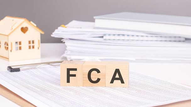 FCA text on a wooden blocks on chart background with a small wooden model house - Photo, Image