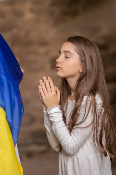 Meisje biddend gewikkeld in Oekraïense vlag. - Foto, afbeelding