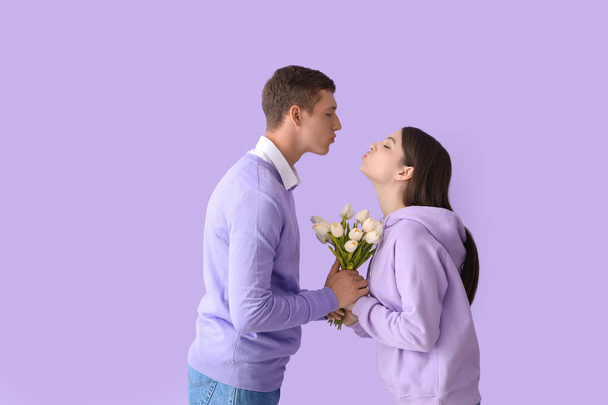Happy young couple with tulips kissing on lilac background - Photo, Image