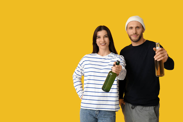 黄色の背景に冷たいビールのボトルが付いている美しい若いカップル - 写真・画像