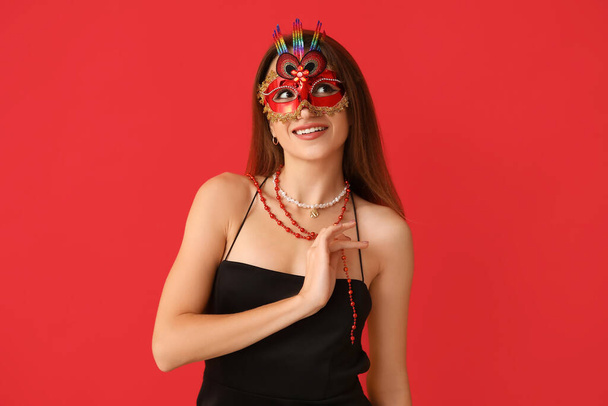 Šťastná mladá žena v karnevalové masce na červeném pozadí - Fotografie, Obrázek