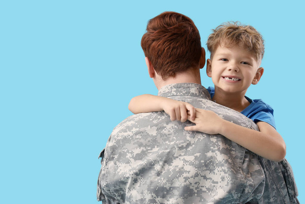 Pieni poika halaa sotilasisäänsä sinisellä taustalla, lähikuva - Valokuva, kuva