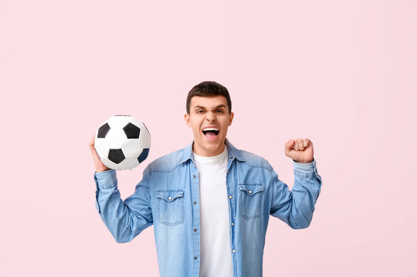 Jeune homme émotionnel avec ballon de football sur fond rose - Photo, image