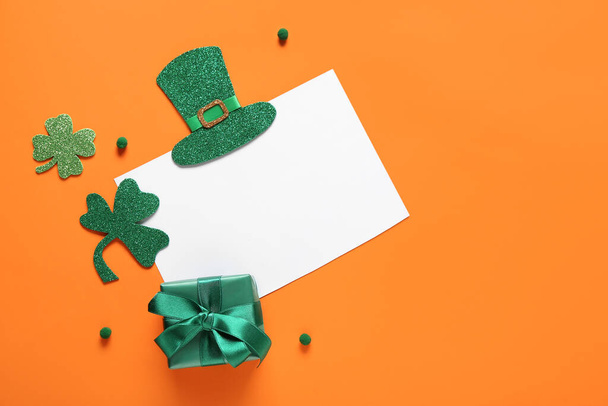 Blanco kaart met geschenkdoos en decor op oranje achtergrond. St. Patrick 's Day viering - Foto, afbeelding