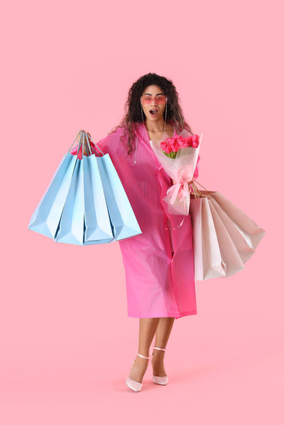 ピンクの背景に花束とショッピングバッグの花束を持つファッショナブルなアフリカ系アメリカ人女性. 国際女性デーのお祝い - 写真・画像