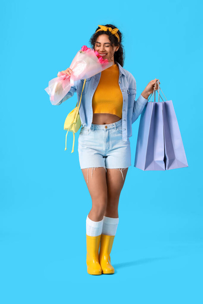 Модная афроамериканка с букетом цветов и сумками для покупок на голубом фоне. Международный женский день - Фото, изображение