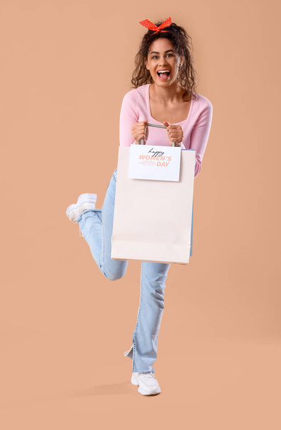Modna Afroamerykanka trzymająca torby na zakupy z kartką z życzeniami na beżowym tle. Międzynarodowy Dzień Kobiet - Zdjęcie, obraz