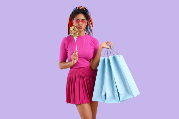 Mujer afroamericana de moda con globo en forma de figura 8 y bolsas de compras sobre fondo lila. Celebración del Día Internacional de la Mujer - Foto, Imagen