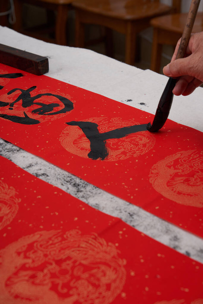 Ένας παλιός καλλιγράφος γράφει δίστιχα κατά τη διάρκεια του Κινέζικου Έτους του Δράκου. Μετάφραση: Η άνοιξη γεμίζει τον κόσμο. - Φωτογραφία, εικόνα