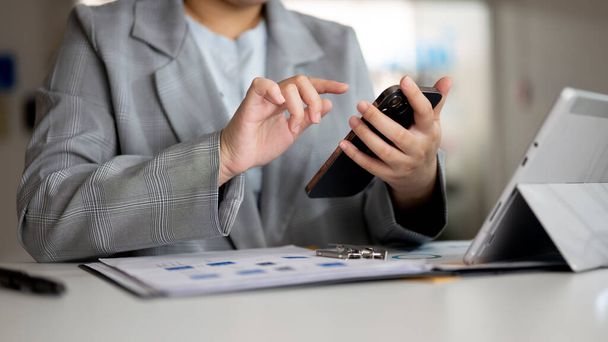 Przycięty obraz azjatyckiej bizneswoman za pomocą smartfona przy biurku w biurze, sprawdzanie wiadomości lub czatowanie. przedsiębiorcy i koncepcje technologii bezprzewodowych - Zdjęcie, obraz