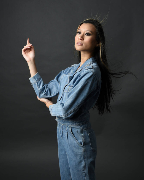 zbliżenie portret brunetka kobieta azjatycki model noszenie casual ubrania, podwójne dżinsy strój. Odizolowany na ciemnym tle studia z cieniami. silny model moda pozowanie. - Zdjęcie, obraz