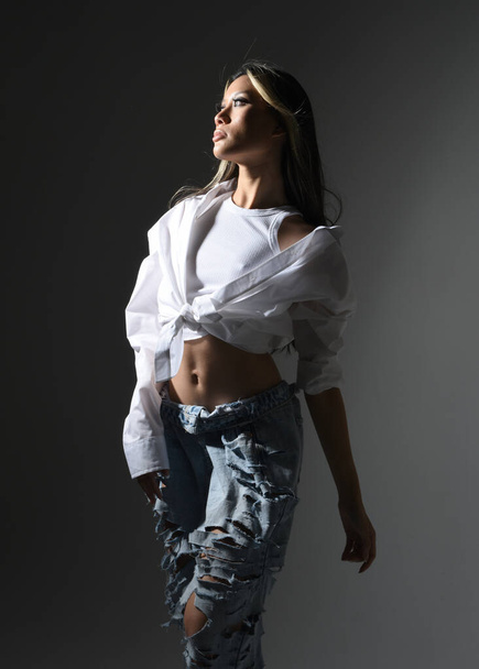 Nahaufnahme Porträt einer brünetten asiatischen Model trägt lässige Kleidung, doppelte Jeans-Outfit. Vereinzelt auf dunklem Studiohintergrund mit Schatten. Starkes Mode-Model posiert. - Foto, Bild