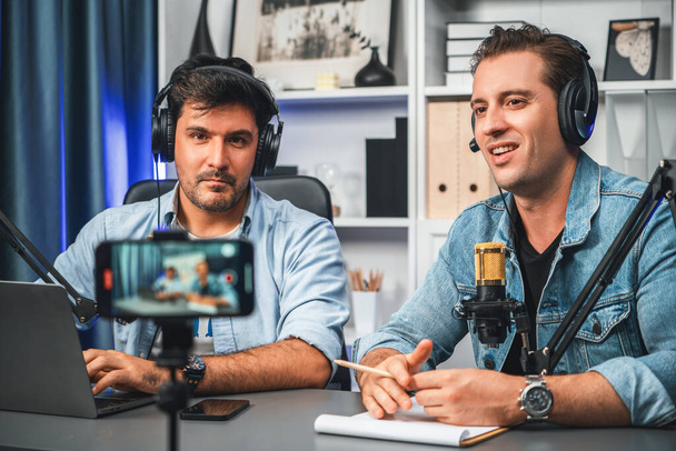 Host channel of creative broadcaster living by smartphone in positive podcast with special guest in list script to advice listeners, wearing headsets, using mic radio record at studio. Sellable. - Photo, Image