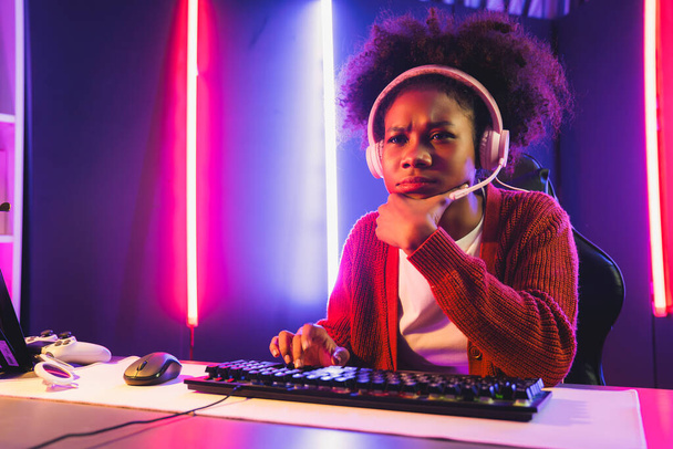Африканська американська дівчина стример грає в онлайн-бої з досвідченою командою Esport в навушниках в неоновому кольоровому освітленні. Говорячи про інших гравців, які планують стратегії, щоб виграти конкурентів. Смаколик. - Фото, зображення