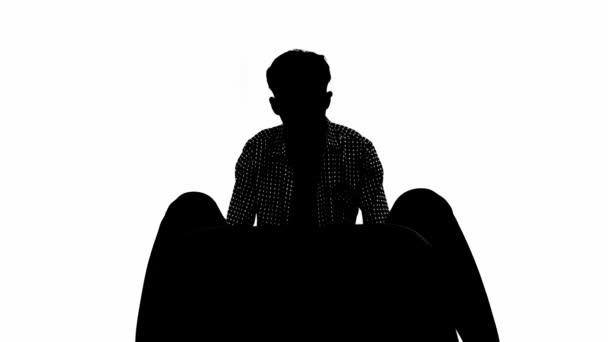 Sylwetka osoby siedzącej z głową w dłoni na białym tle, przedstawiająca smutek lub depresję wewnątrz białego pokoju - Materiał filmowy, wideo