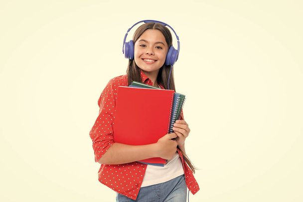 Back to school. Schoolgirl student in headphones with school bag backpack hold book on isolated studio background. School and education concept. Portrait of happy smiling teenage child girl - Photo, Image
