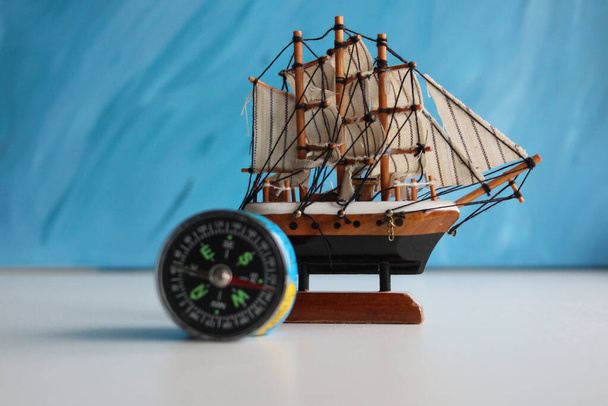 Drewniany model żaglowca i zabytkowy kompas na białej powierzchni na niebieskim tle    - Zdjęcie, obraz