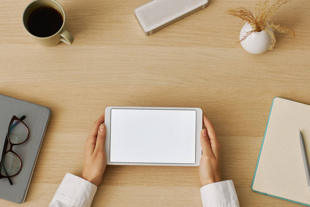 Vista superior mínima de manos femeninas sosteniendo tableta digital con maqueta de pantalla blanca en el lugar de trabajo del escritorio, espacio de copia - Foto, Imagen