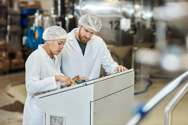 Portrait de deux travailleurs portant des blouses de laboratoire faisant fonctionner l'équipement à l'usine alimentaire, espace de copie - Photo, image