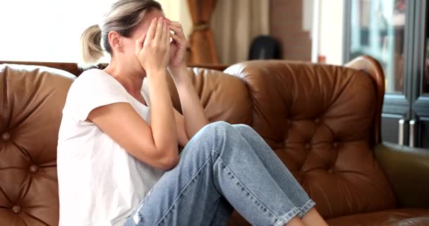 Γυναίκα αισθάνεται αναστατωμένος κάθεται στον καναπέ στο σπίτι. Λυπημένη δυστυχισμένη ή απογοητευμένη κλαίγοντας μόνη στο δωμάτιο - Πλάνα, βίντεο