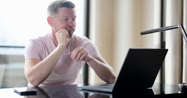 Uomo annoiato controllare i contenuti del computer portatile online seduto sul tavolo a casa. Emozioni nervose di attesa e delusione - Filmati, video