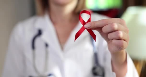 Γιατρός κρατά στο χέρι κόκκινη κορδέλα σύμβολο της διεθνούς ημέρας για την προστασία των ανθρώπων από το AIDS και HIV. Βλάβη στο ανοσοποιητικό σύστημα με την ανάπτυξη συνδρόμου επίκτητης ανοσοανεπάρκειας - Πλάνα, βίντεο